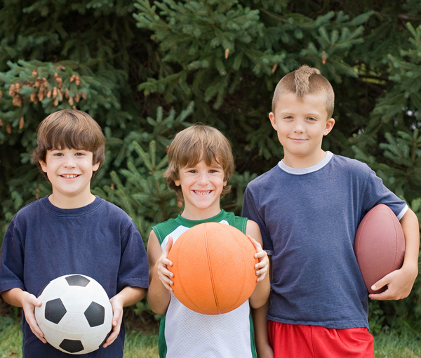 three young boys smiling and playing sports